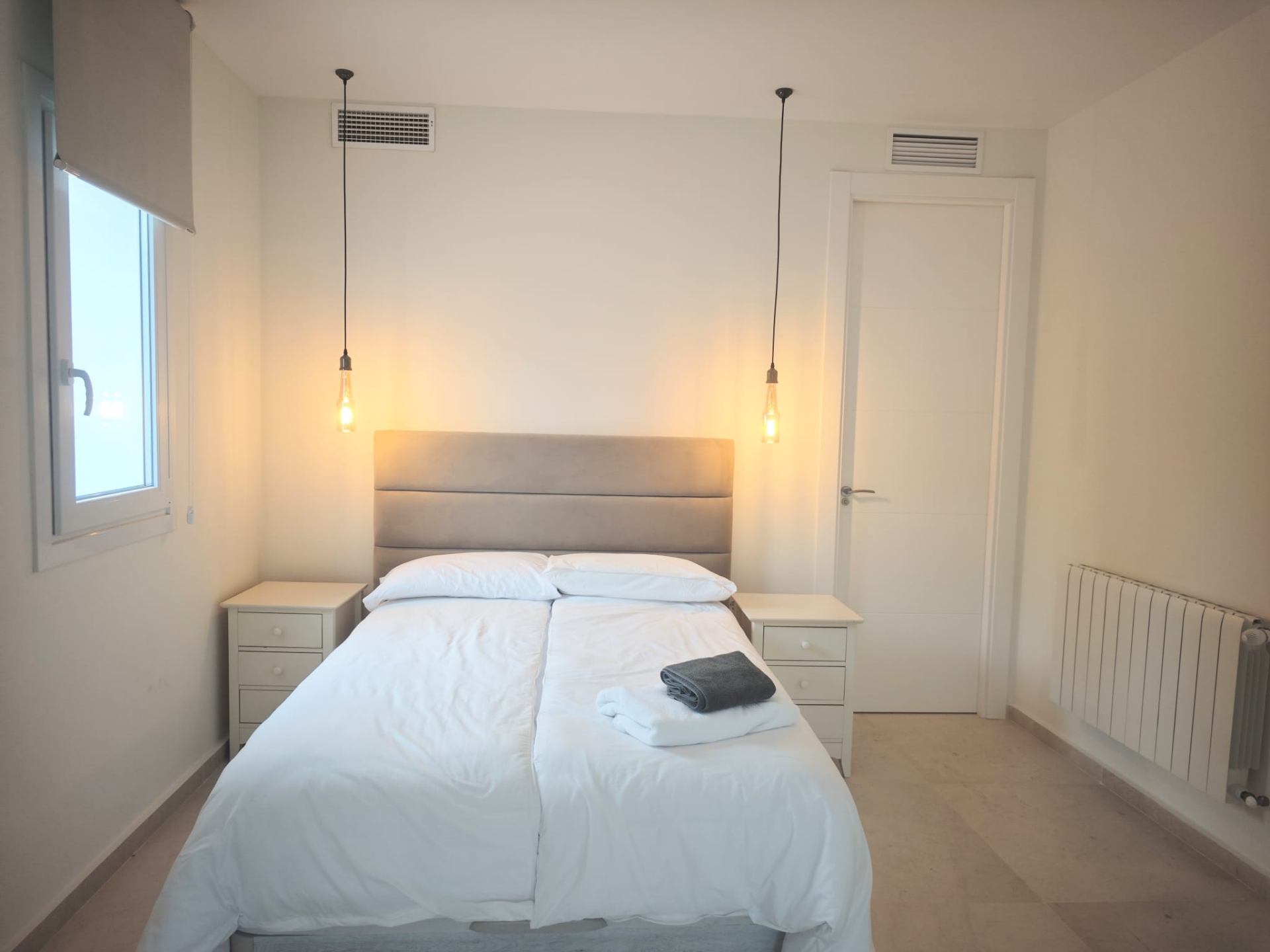 Guest bedroom with grey upholstered headboard and pendant lighting
